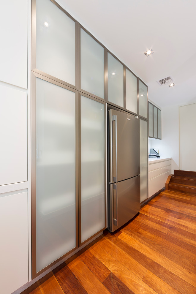 Inspiration for a medium sized modern kitchen pantry in Canberra - Queanbeyan with glass-front cabinets, stainless steel cabinets, engineered stone countertops, white splashback, glass sheet splashback, light hardwood flooring, brown floors and white worktops.