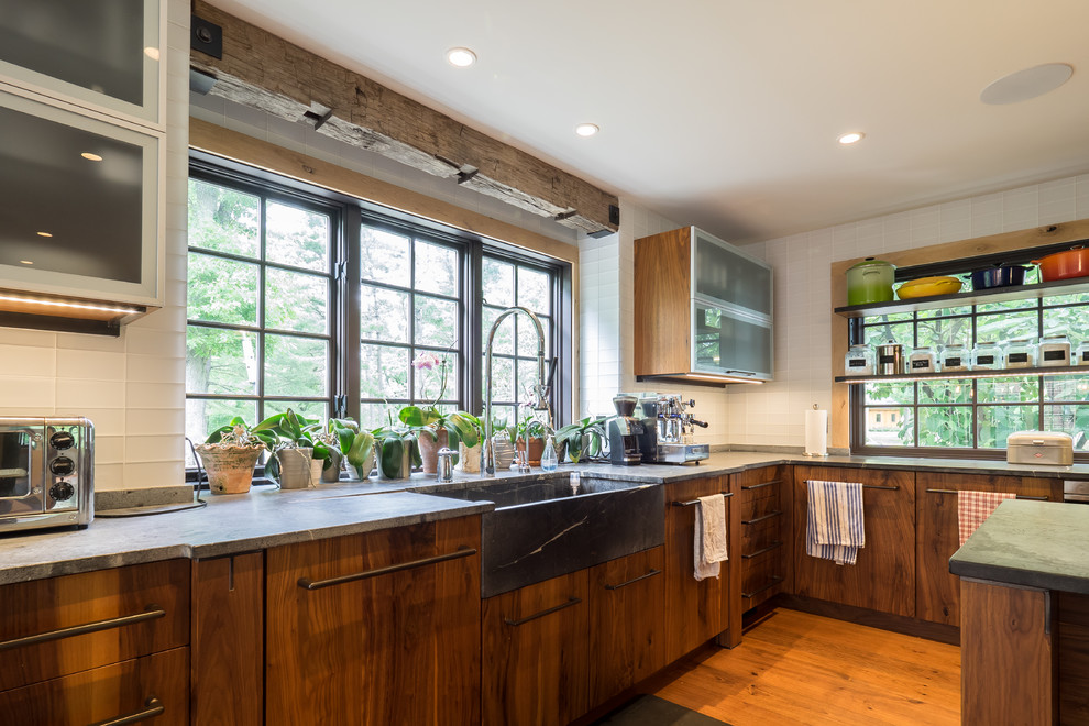 This is an example of a medium sized rustic galley enclosed kitchen in Philadelphia with a belfast sink, open cabinets, medium wood cabinets, soapstone worktops, white splashback, stainless steel appliances, medium hardwood flooring, an island, brown floors and glass tiled splashback.