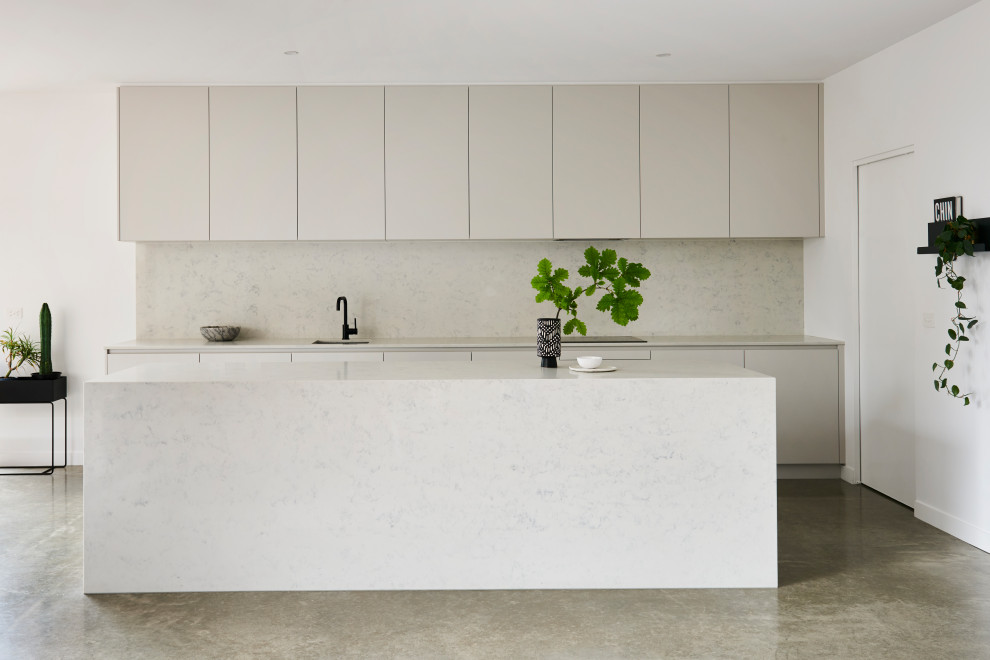 Foto på ett mellanstort funkis vit kök, med släta luckor, grå skåp, bänkskiva i kvarts, vitt stänkskydd, betonggolv, en köksö, grått golv, en undermonterad diskho och stänkskydd i sten