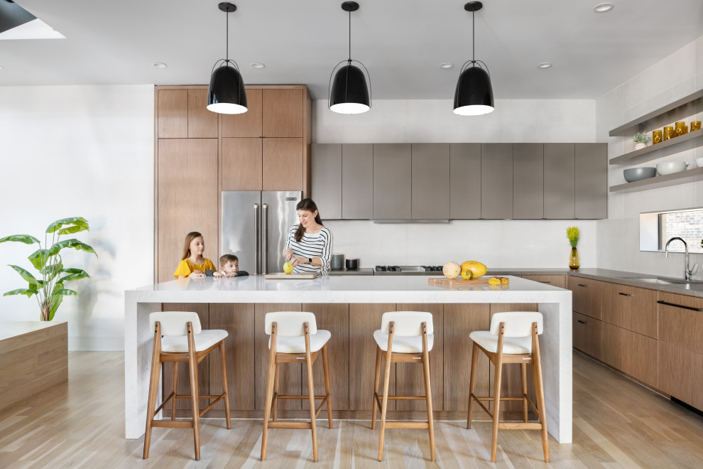 Mid-sized trendy l-shaped light wood floor and brown floor open concept kitchen photo in Houston with an undermount sink, flat-panel cabinets, medium tone wood cabinets, quartz countertops, white backsplash, porcelain backsplash, stainless steel appliances, an island and white countertops