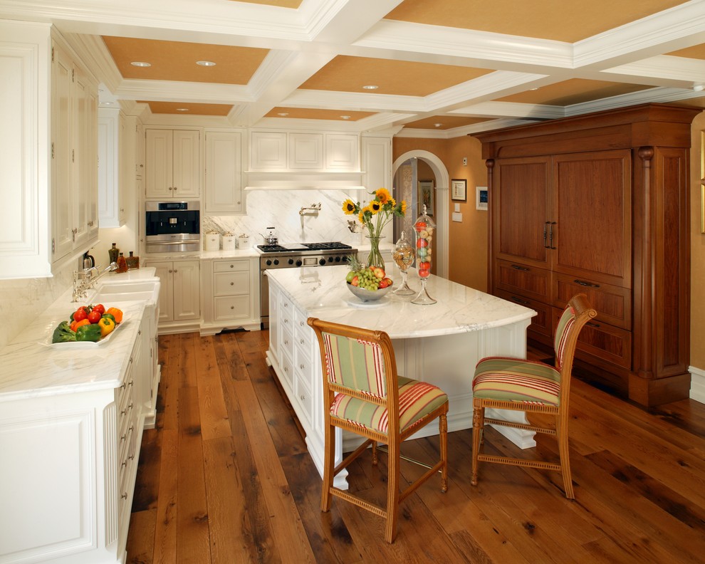 Kitchen - large traditional l-shaped medium tone wood floor kitchen idea in Philadelphia with a farmhouse sink, white cabinets, marble countertops, white backsplash, stone slab backsplash, stainless steel appliances, raised-panel cabinets and an island