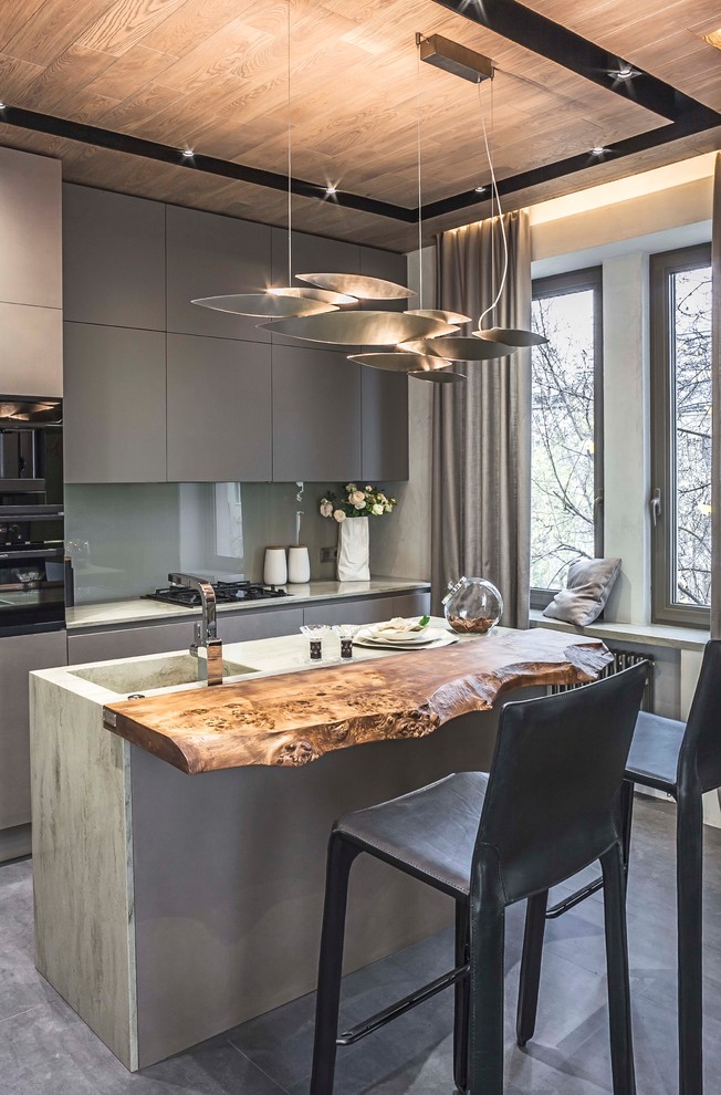 Trendy galley concrete floor and gray floor open concept kitchen photo in New York with an integrated sink, flat-panel cabinets, gray cabinets, concrete countertops, gray backsplash, glass sheet backsplash, black appliances and an island