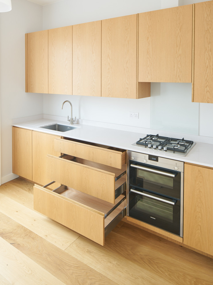 Photo of a medium sized modern single-wall kitchen in London with an integrated sink, flat-panel cabinets, light wood cabinets, composite countertops, light hardwood flooring and no island.