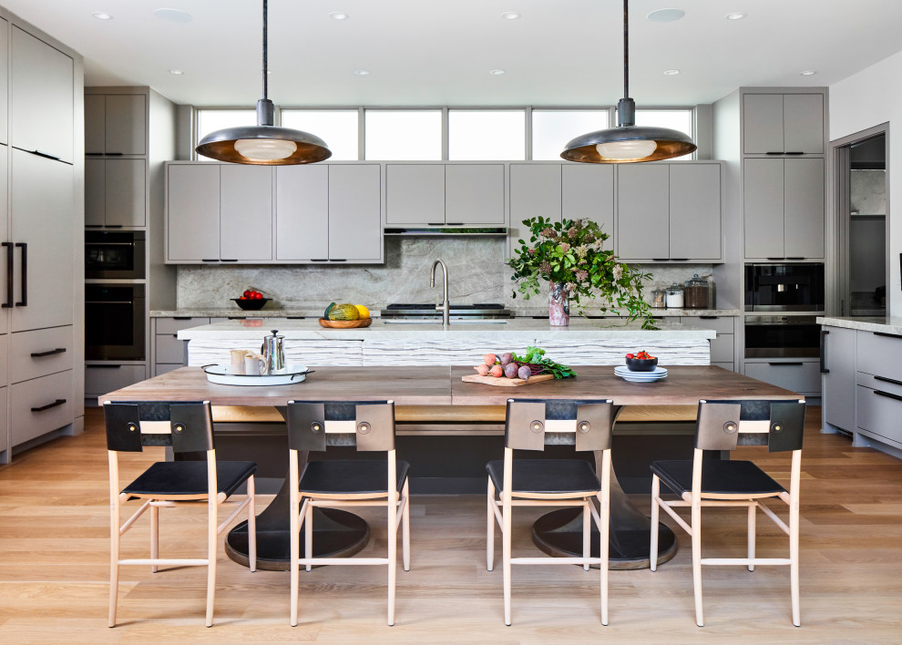 This is an example of a contemporary u-shaped kitchen/diner in Dallas with a submerged sink, flat-panel cabinets, grey cabinets, grey splashback, stone slab splashback, stainless steel appliances, light hardwood flooring, an island, beige floors and grey worktops.