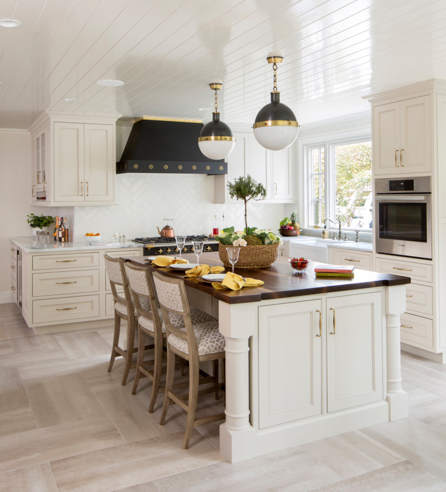 Inredning av ett klassiskt vit vitt l-kök, med en rustik diskho, luckor med profilerade fronter, vita skåp, vitt stänkskydd, rostfria vitvaror, en köksö och beiget golv
