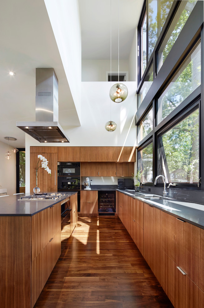 Inspiration for a large modern l-shaped kitchen/diner in Philadelphia with a double-bowl sink, flat-panel cabinets, medium wood cabinets, composite countertops, grey splashback, stone slab splashback, stainless steel appliances, medium hardwood flooring, an island and brown floors.