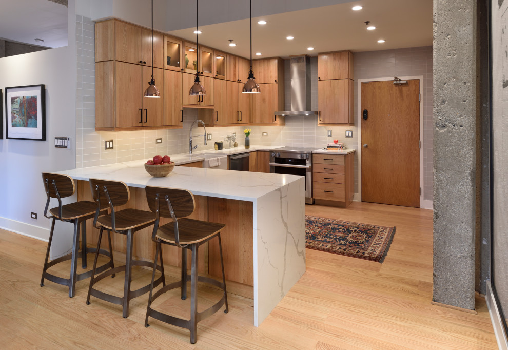 シカゴにあるインダストリアルスタイルのおしゃれなキッチン (エプロンフロントシンク、フラットパネル扉のキャビネット、中間色木目調キャビネット、グレーのキッチンパネル、シルバーの調理設備、淡色無垢フローリング、ベージュの床、白いキッチンカウンター) の写真