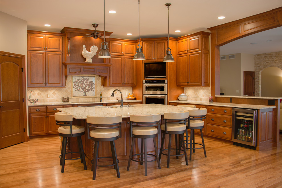 Foto de cocina tradicional grande con fregadero bajoencimera, armarios con paneles con relieve, puertas de armario de madera oscura, electrodomésticos de acero inoxidable, suelo de madera clara, una isla, encimera de cuarzo compacto, salpicadero beige y salpicadero de azulejos de piedra