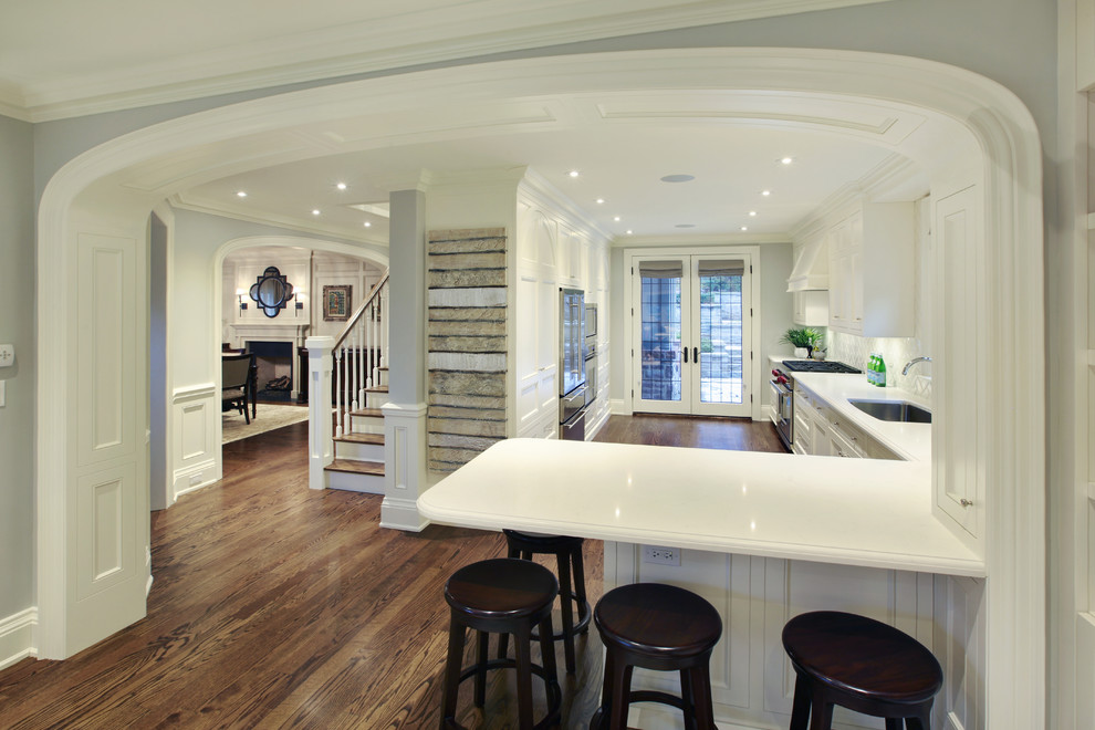 Inspiration for a mid-sized transitional l-shaped medium tone wood floor kitchen remodel in Toronto with an undermount sink, recessed-panel cabinets, white cabinets, white backsplash and stainless steel appliances