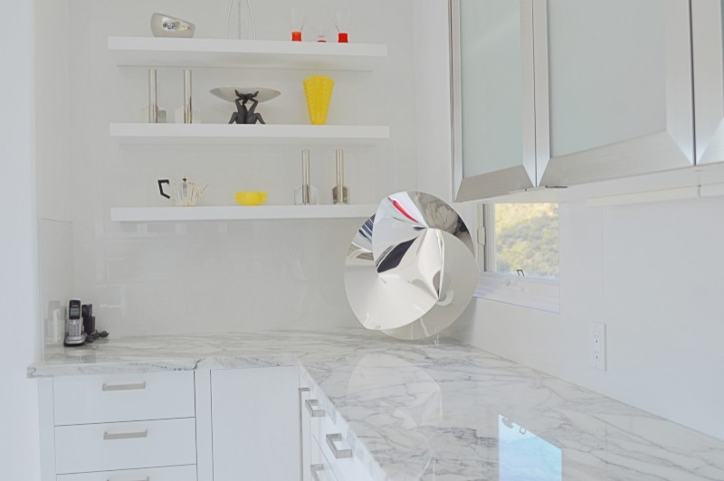 Photo of a medium sized contemporary l-shaped kitchen in Los Angeles with a submerged sink, flat-panel cabinets, white cabinets, marble worktops, white splashback, glass sheet splashback, stainless steel appliances, an island and white floors.
