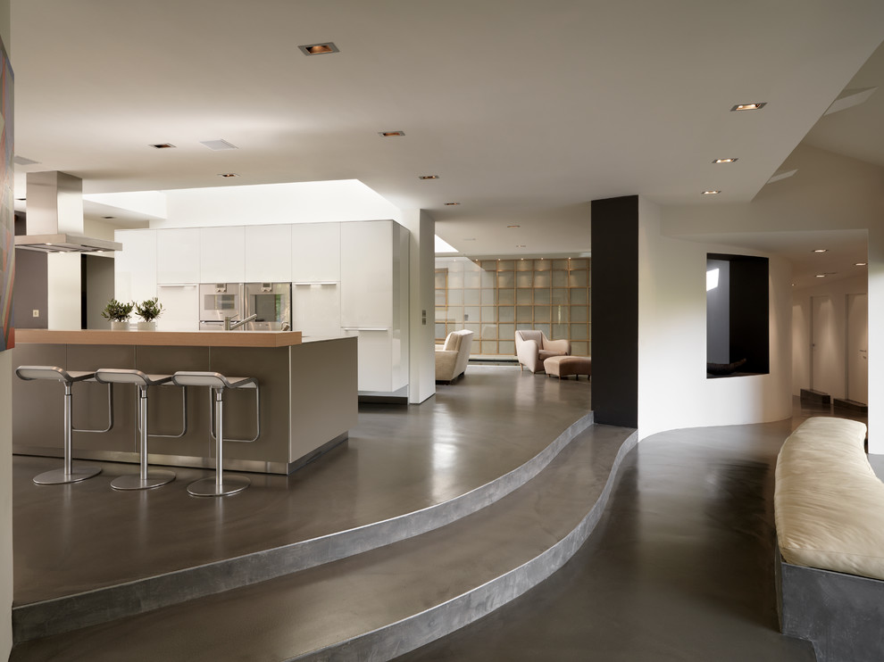 Cette photo montre une cuisine ouverte parallèle tendance avec un placard à porte plane, des portes de placard blanches, un électroménager en acier inoxydable, sol en béton ciré et îlot.