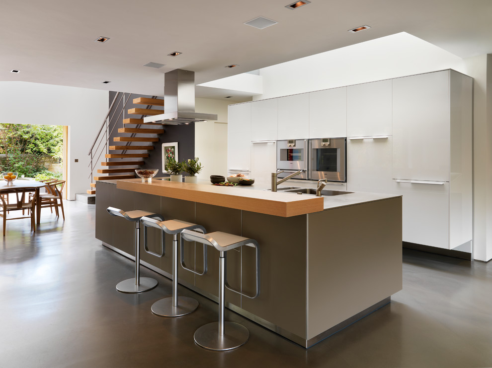 Идея дизайна: параллельная кухня в современном стиле с обеденным столом, монолитной мойкой, плоскими фасадами, белыми фасадами, техникой из нержавеющей стали, бетонным полом и островом
