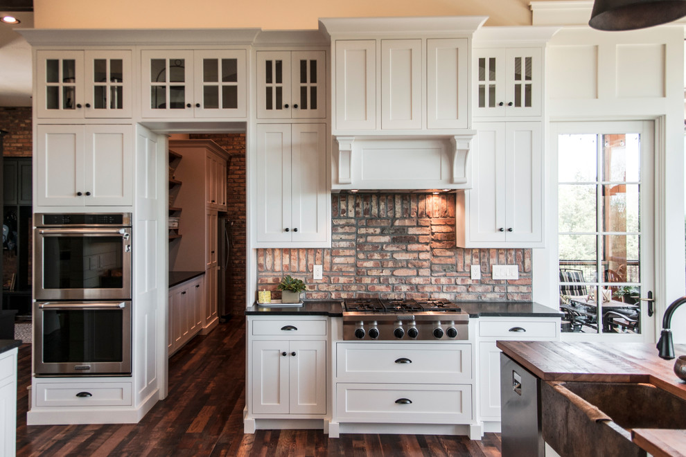Inspiration for a huge timeless l-shaped dark wood floor open concept kitchen remodel in Other with an undermount sink, raised-panel cabinets, white cabinets, onyx countertops, red backsplash, brick backsplash, stainless steel appliances and an island