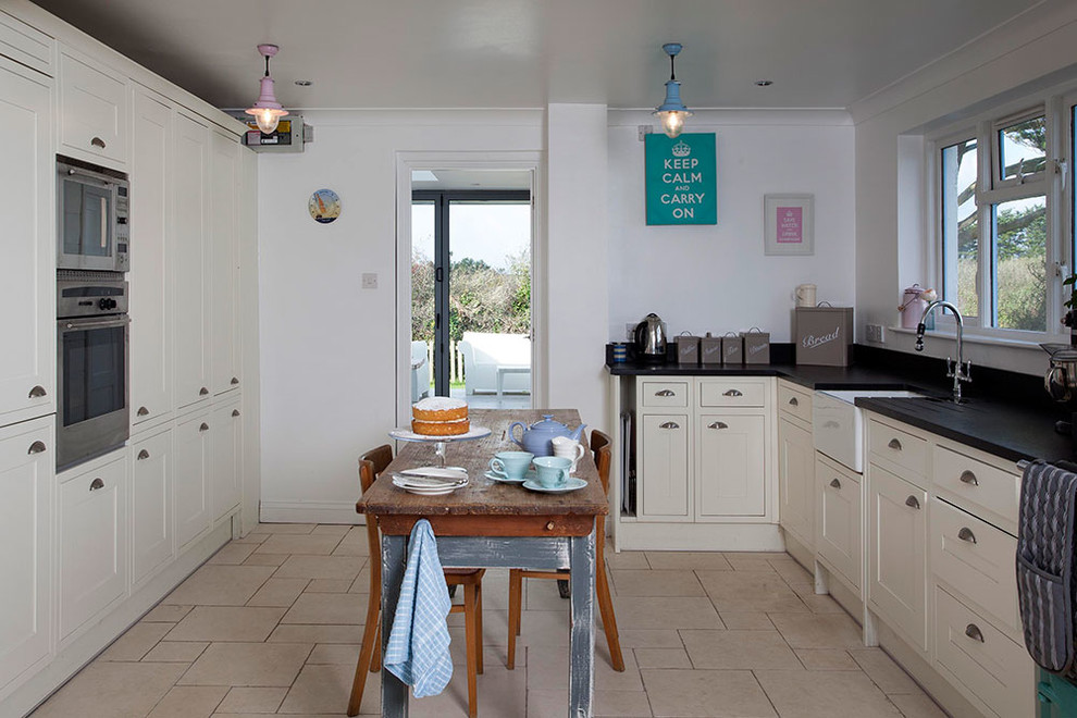 Photo of a small beach style galley open plan kitchen in Cornwall with a belfast sink, flat-panel cabinets, white cabinets, composite countertops, black splashback, ceramic splashback, coloured appliances, ceramic flooring and no island.