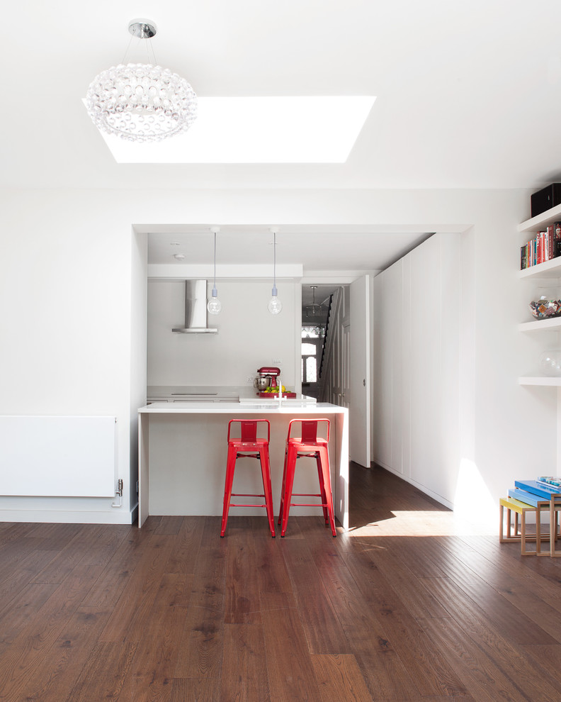 Mittelgroße, Geschlossene Moderne Küche in U-Form mit braunem Holzboden, flächenbündigen Schrankfronten, weißen Schränken und Kücheninsel in London