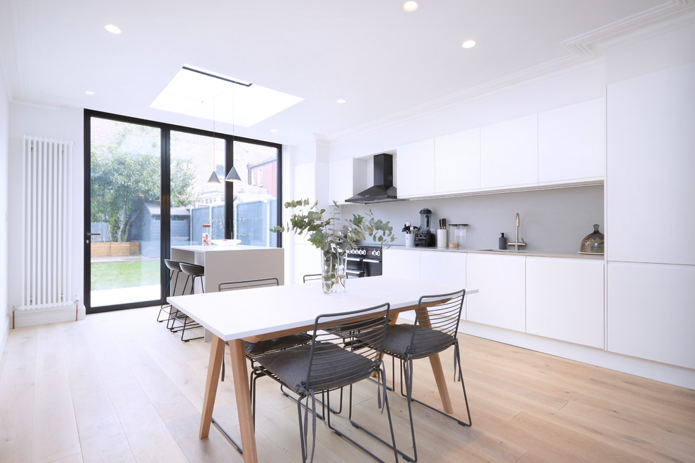 Contemporary single-wall kitchen/diner in London with a submerged sink, flat-panel cabinets, white cabinets, beige splashback, black appliances, light hardwood flooring, an island, beige floors and beige worktops.
