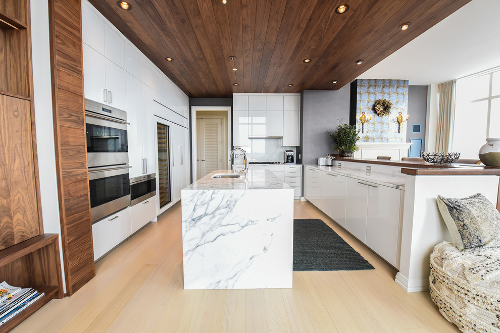 Immagine di una cucina ad ambiente unico design con lavello sottopiano, ante lisce, ante bianche, paraspruzzi grigio, parquet chiaro, 2 o più isole, pavimento beige e top grigio