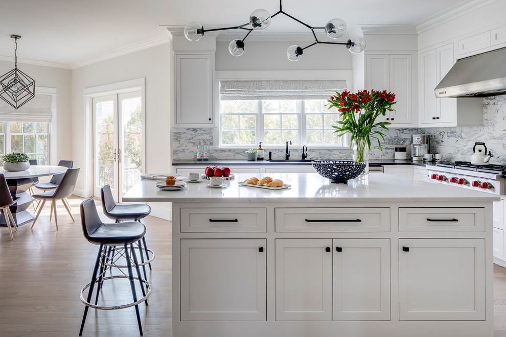 Inspiration for a medium sized contemporary u-shaped kitchen/diner in New York with recessed-panel cabinets, white cabinets, engineered stone countertops, marble splashback, stainless steel appliances, light hardwood flooring and an island.
