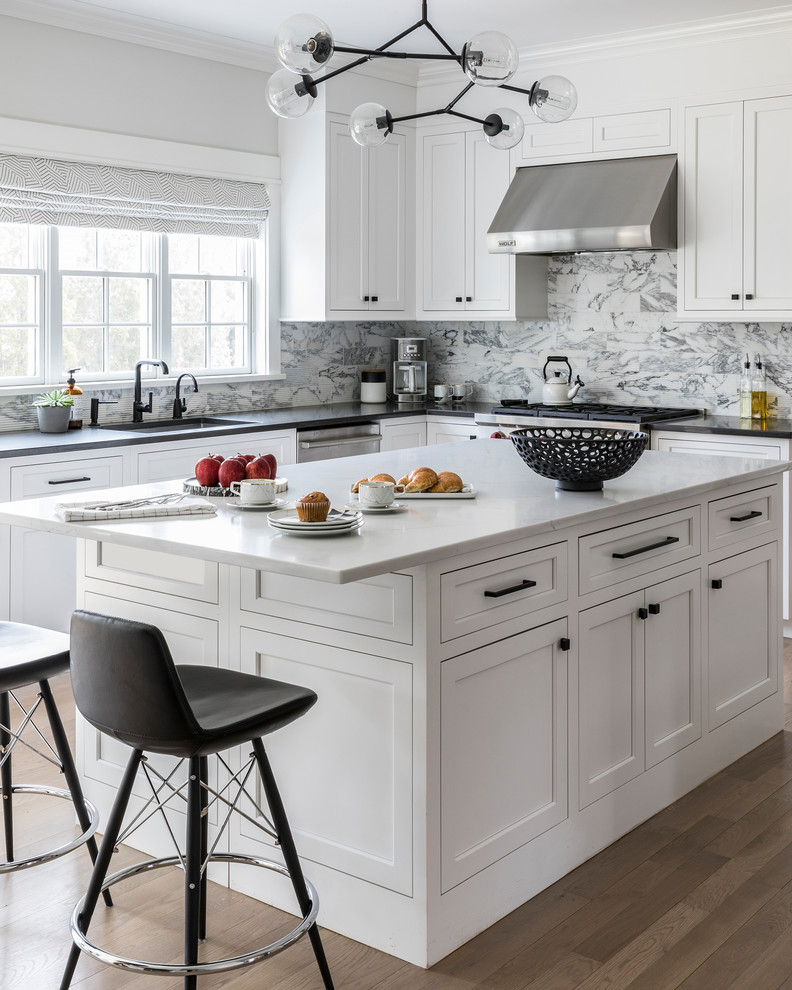 Modern inredning av ett mellanstort kök, med luckor med infälld panel, vita skåp, bänkskiva i kvarts, stänkskydd i marmor, rostfria vitvaror, ljust trägolv och en köksö