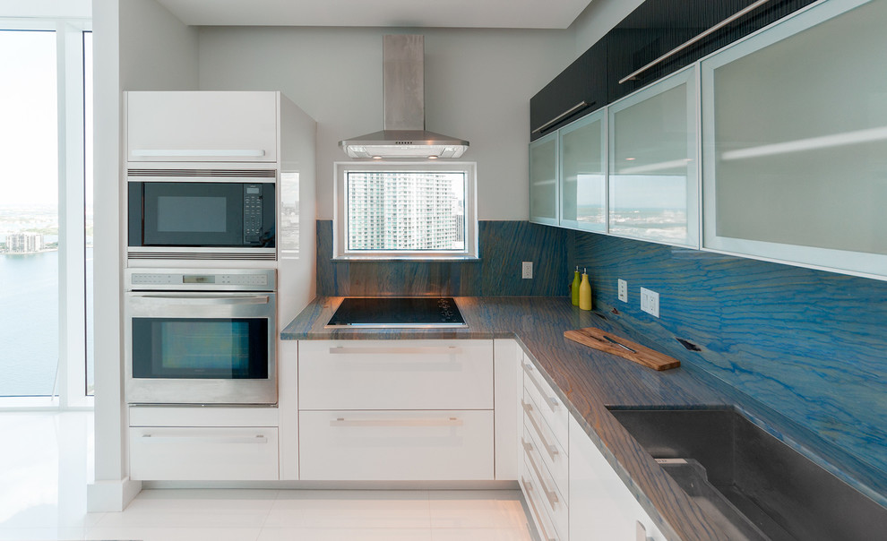 Moderne Wohnküche in L-Form mit Unterbauwaschbecken, Glasfronten, weißen Schränken, Quarzit-Arbeitsplatte, Küchenrückwand in Blau, Rückwand aus Stein und Küchengeräten aus Edelstahl in Miami