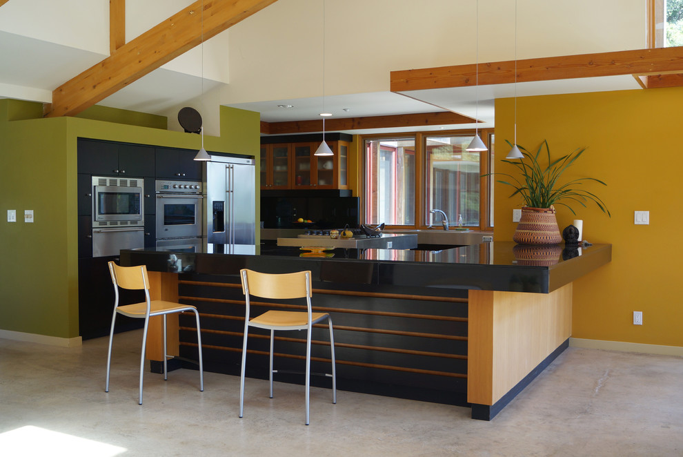 Foto på ett stort funkis u-kök, med släta luckor, svarta skåp, svart stänkskydd, rostfria vitvaror, betonggolv och en halv köksö