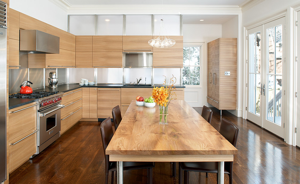 Пример оригинального дизайна: угловая кухня в современном стиле с обеденным столом, плоскими фасадами, светлыми деревянными фасадами и техникой из нержавеющей стали