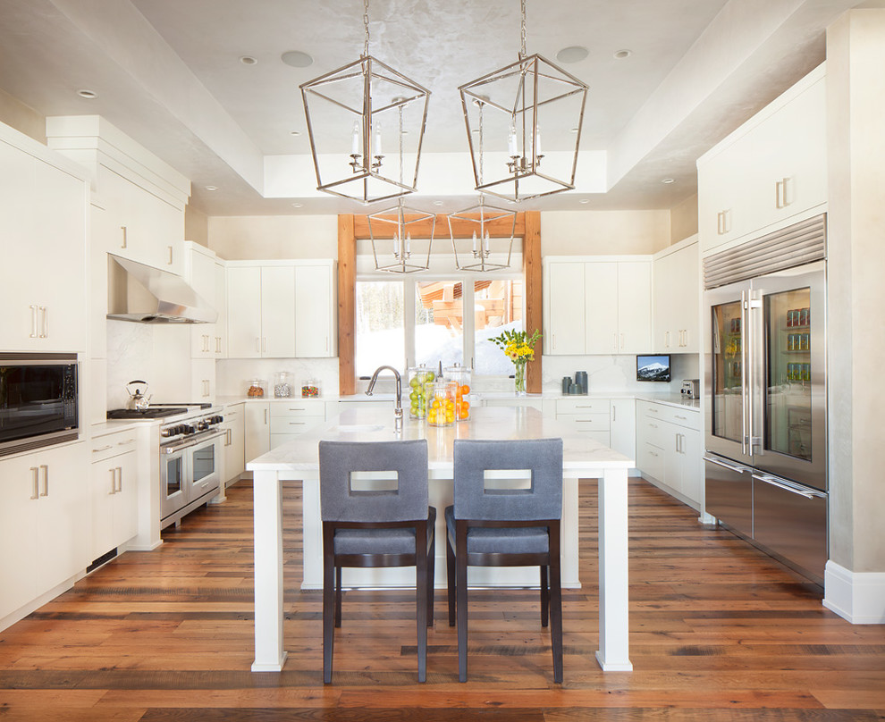 Eat-in kitchen - large transitional u-shaped medium tone wood floor eat-in kitchen idea in Salt Lake City with a farmhouse sink, flat-panel cabinets, white cabinets, solid surface countertops, white backsplash, stone slab backsplash, stainless steel appliances and an island
