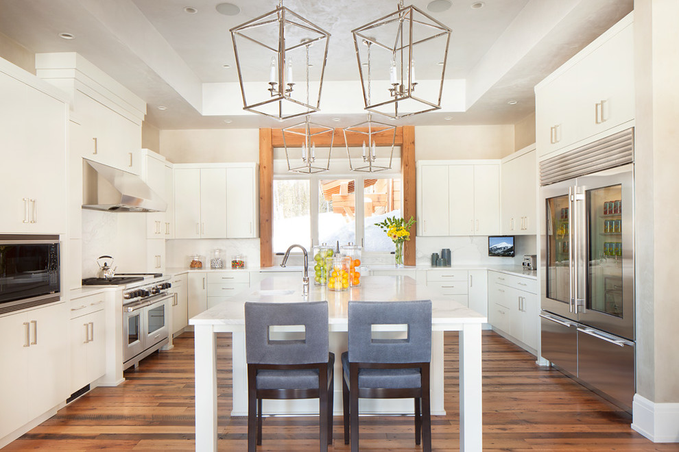 Photo of a medium sized classic u-shaped kitchen/diner in Salt Lake City with flat-panel cabinets, white cabinets, white splashback, stainless steel appliances, medium hardwood flooring, an island, a double-bowl sink, composite countertops and stone slab splashback.