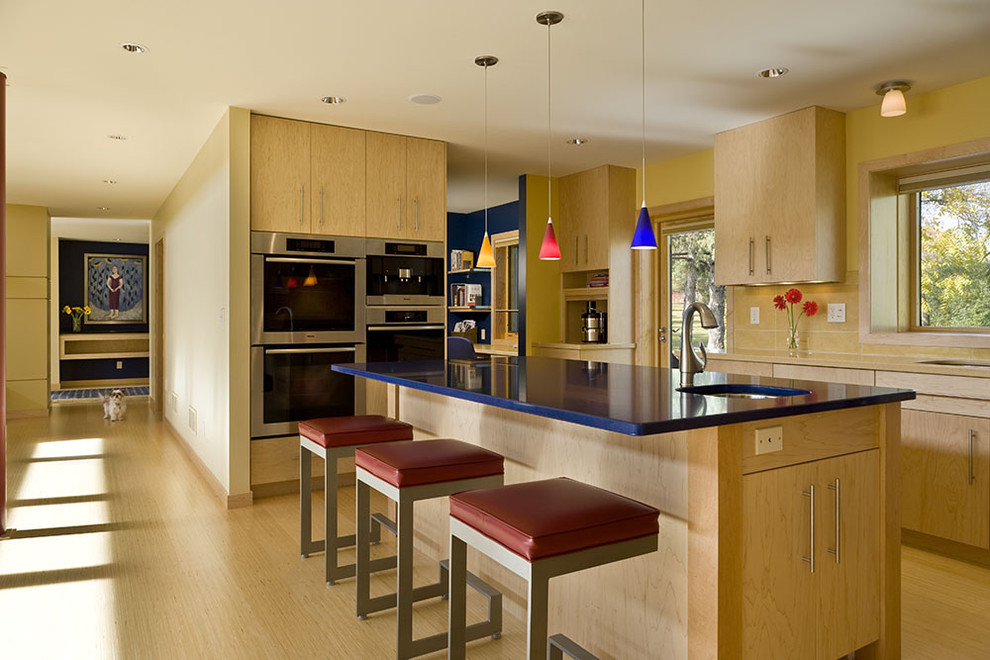 На фото: кухня в современном стиле с техникой из нержавеющей стали, плоскими фасадами, светлыми деревянными фасадами и синей столешницей с