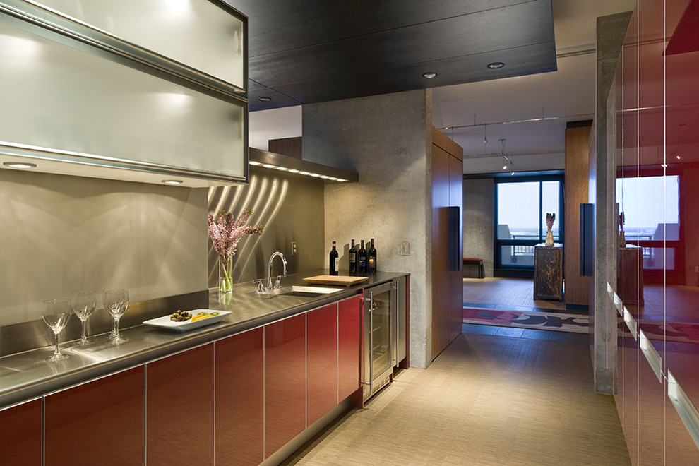This is an example of a contemporary galley enclosed kitchen in Minneapolis with a submerged sink, flat-panel cabinets, red cabinets, stainless steel worktops, stainless steel appliances, metallic splashback and metal splashback.