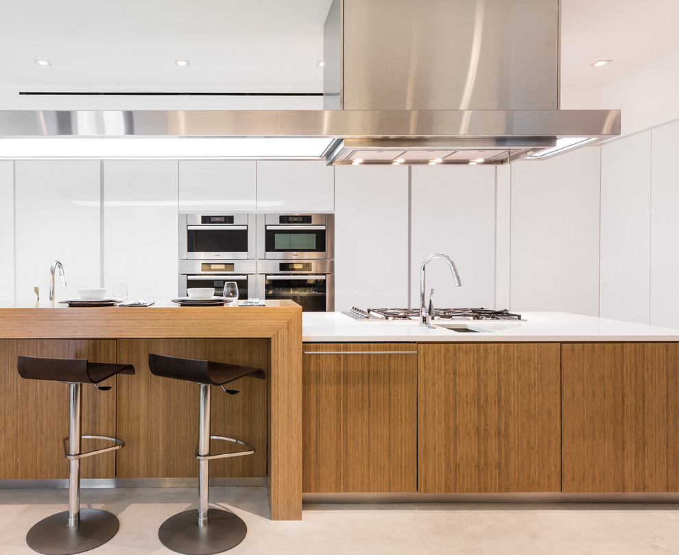 This is an example of an expansive modern u-shaped open plan kitchen in Miami with a submerged sink, flat-panel cabinets, white cabinets, engineered stone countertops, white splashback, stone slab splashback, stainless steel appliances, limestone flooring, an island, beige floors and white worktops.
