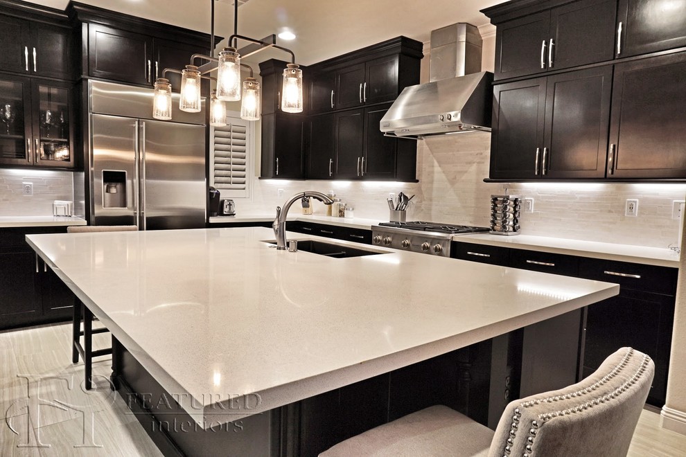 Example of a large transitional l-shaped limestone floor open concept kitchen design in Las Vegas with an undermount sink, shaker cabinets, black cabinets, quartz countertops, white backsplash, stone tile backsplash, stainless steel appliances and an island