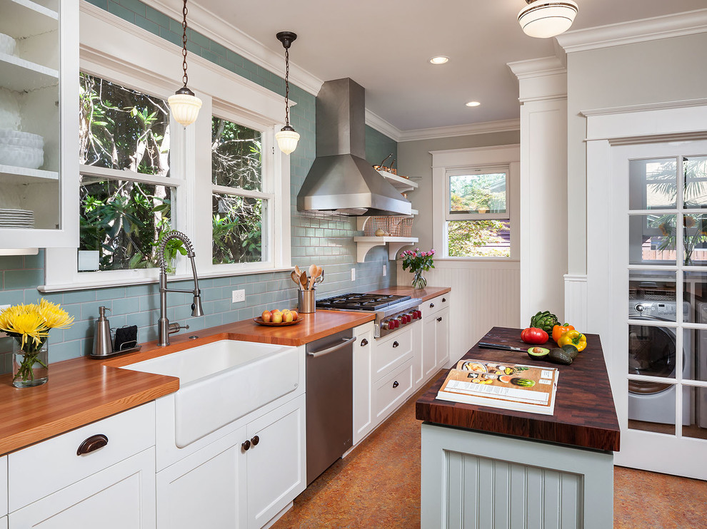Foto på ett lantligt linjärt kök, med en rustik diskho, skåp i shakerstil, vita skåp, träbänkskiva, blått stänkskydd, stänkskydd i tunnelbanekakel, rostfria vitvaror och en köksö