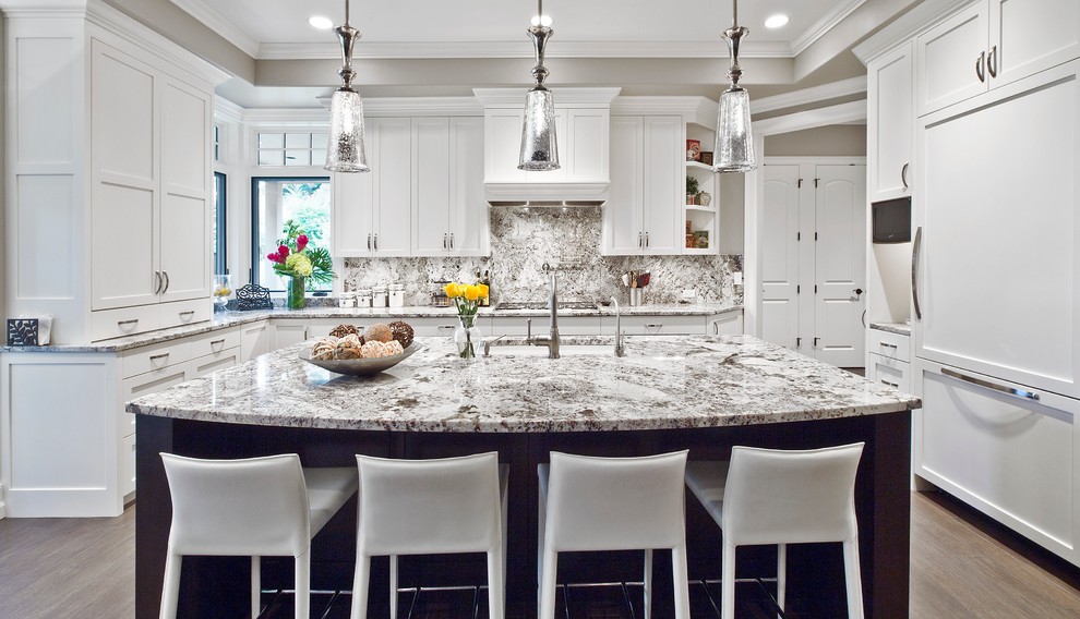 Exempel på ett klassiskt u-kök, med skåp i shakerstil, vita skåp, integrerade vitvaror, mellanmörkt trägolv, en köksö, en undermonterad diskho, granitbänkskiva, stänkskydd i sten, grått stänkskydd och brunt golv
