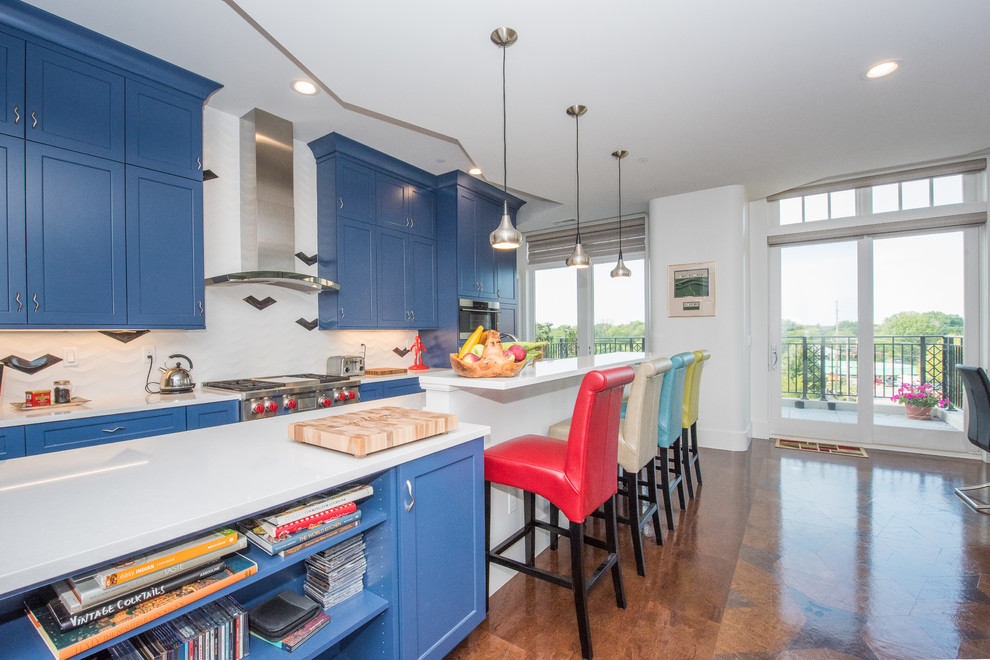Inredning av ett modernt kök, med en undermonterad diskho, luckor med infälld panel, blå skåp, bänkskiva i kvarts, vitt stänkskydd, stänkskydd i porslinskakel, rostfria vitvaror, korkgolv, en köksö och brunt golv