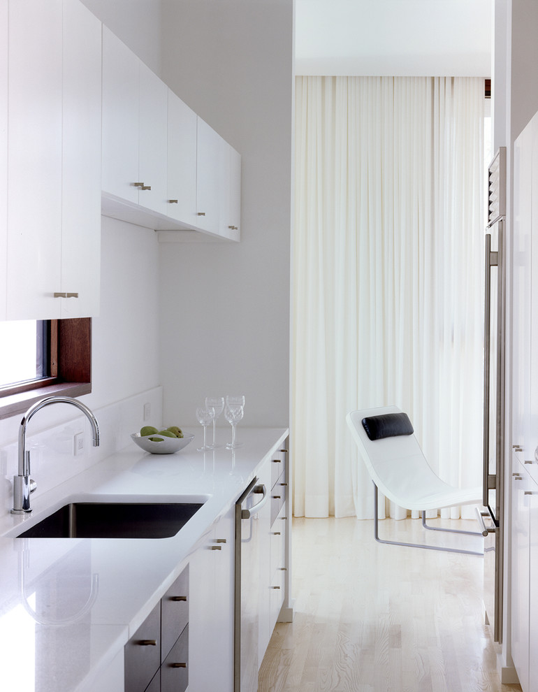 Diseño de cocina moderna con armarios con paneles lisos, puertas de armario blancas y suelo de madera clara