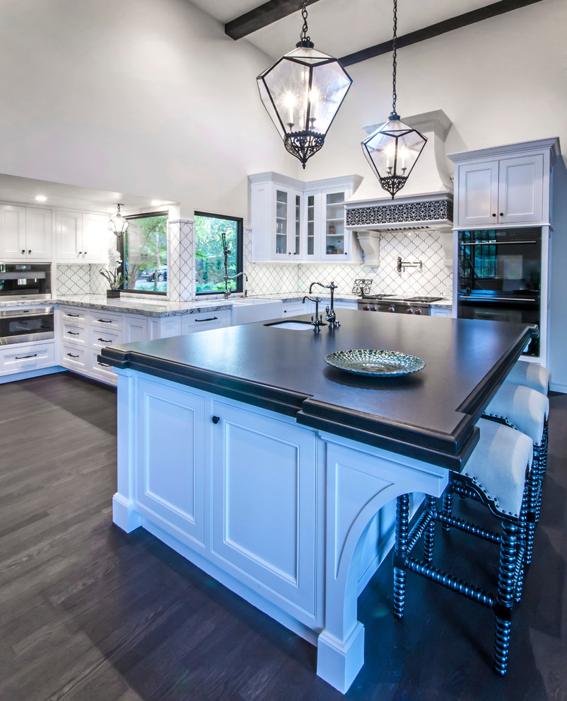 Example of a huge tuscan l-shaped dark wood floor open concept kitchen design in Santa Barbara with an undermount sink, flat-panel cabinets, white cabinets, granite countertops, white backsplash, ceramic backsplash, stainless steel appliances and an island