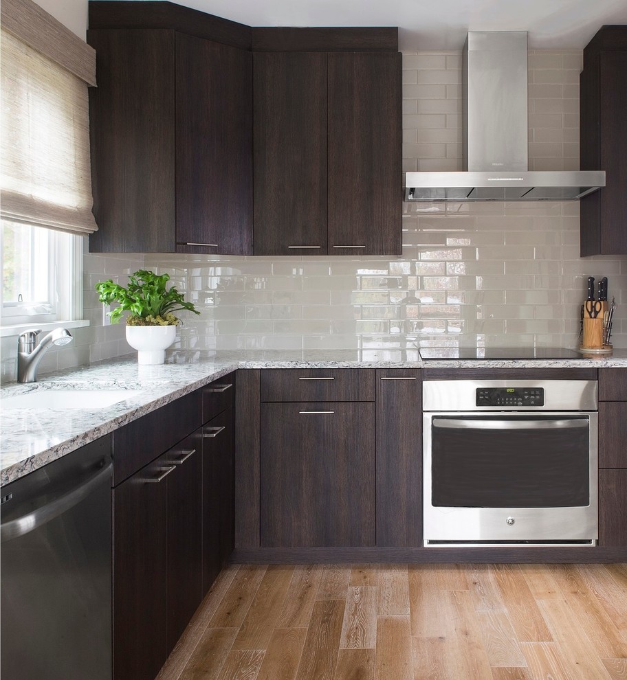 Mid-sized trendy u-shaped light wood floor enclosed kitchen photo in New York with an undermount sink, flat-panel cabinets, dark wood cabinets, solid surface countertops, gray backsplash, glass tile backsplash and stainless steel appliances