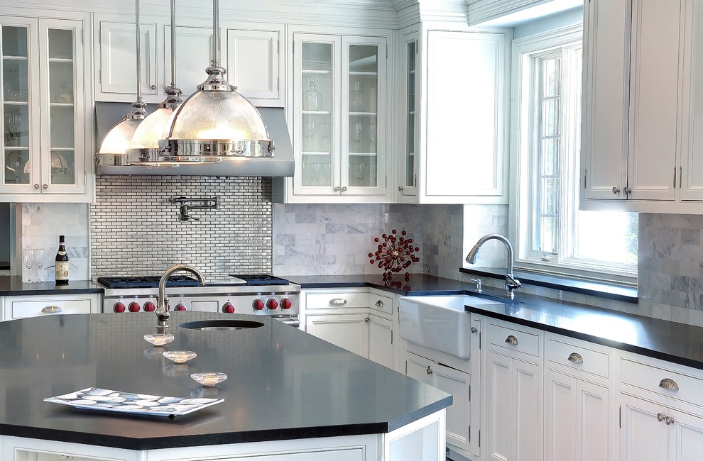 Elegant l-shaped kitchen photo in New York with a farmhouse sink, white cabinets, soapstone countertops, stainless steel appliances, an island, glass-front cabinets, metallic backsplash and metal backsplash