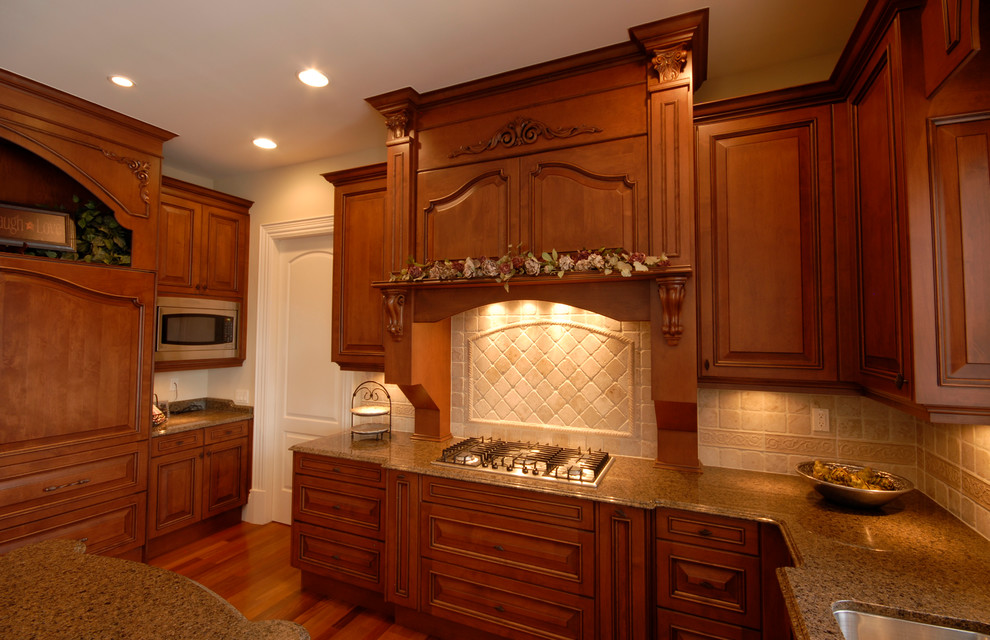 Foto på ett stort vintage kök, med en dubbel diskho, luckor med upphöjd panel, skåp i mellenmörkt trä, granitbänkskiva, beige stänkskydd, stänkskydd i stenkakel, integrerade vitvaror, mellanmörkt trägolv och en köksö