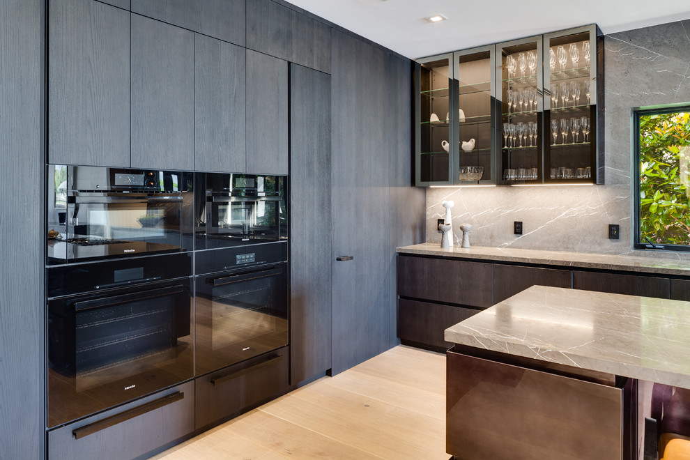 Design ideas for a large contemporary single-wall open plan kitchen in Miami with flat-panel cabinets, blue cabinets, grey splashback, stone slab splashback, black appliances, light hardwood flooring, an island, beige floors and beige worktops.