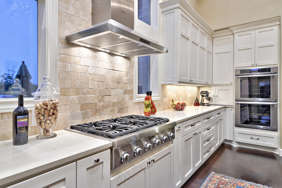 Diseño de cocina comedor clásica con fregadero bajoencimera, puertas de armario blancas, salpicadero de azulejos de piedra, electrodomésticos de acero inoxidable y una isla