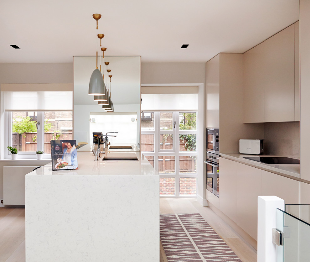 Photo of a scandinavian galley kitchen in London with a double-bowl sink, flat-panel cabinets, quartz worktops, stone slab splashback, stainless steel appliances, light hardwood flooring and a breakfast bar.