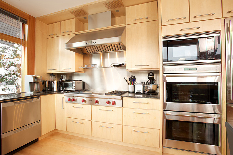 Esempio di una piccola cucina minimal con ante lisce, ante in legno chiaro, top in granito, elettrodomestici in acciaio inossidabile, parquet chiaro e lavello sottopiano
