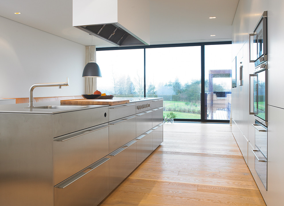 Esempio di una cucina minimalista di medie dimensioni con lavello integrato, ante lisce, ante grigie, top in acciaio inossidabile e parquet chiaro