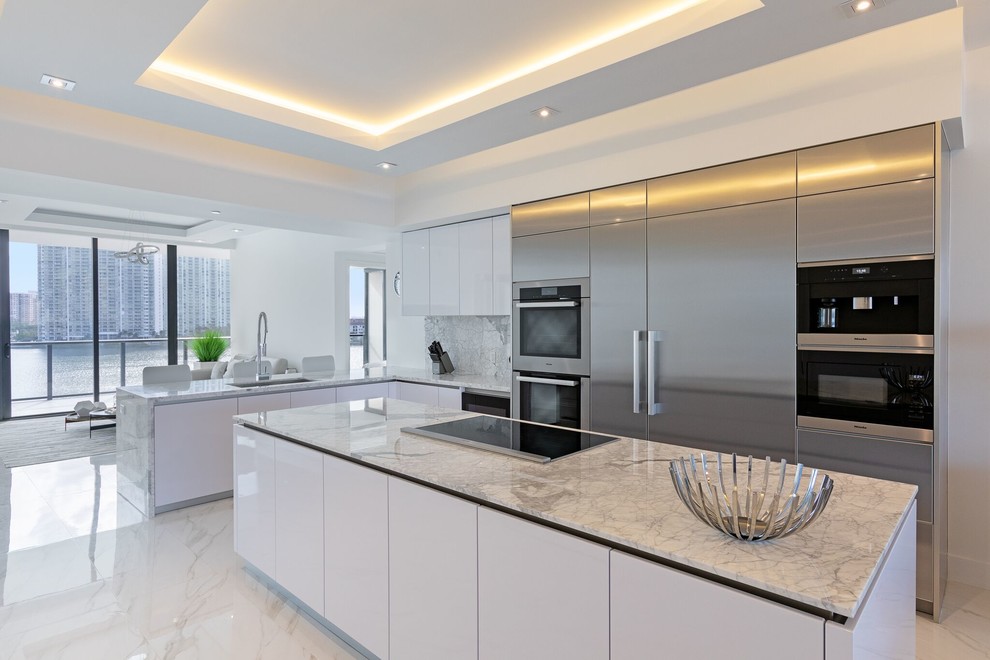 Modern inredning av ett grå grått kök, med en undermonterad diskho, släta luckor, skåp i rostfritt stål, grått stänkskydd, rostfria vitvaror, marmorgolv, en köksö och vitt golv