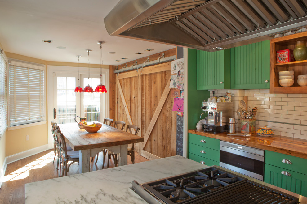 Modelo de cocina comedor clásica con salpicadero de azulejos tipo metro, encimera de madera, puertas de armario verdes y electrodomésticos de acero inoxidable
