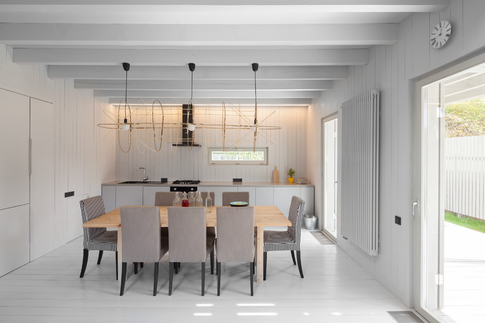 На фото: кухня в скандинавском стиле с обеденным столом, деревянным полом, плоскими фасадами и белыми фасадами в частном доме