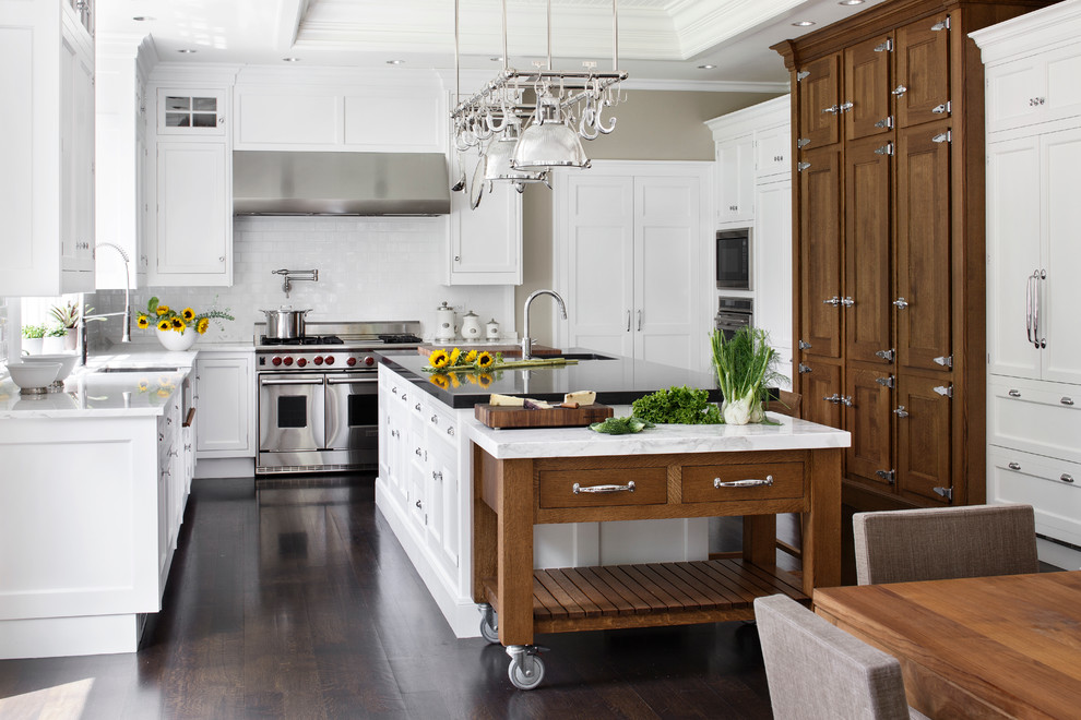 Inspiration for a large timeless u-shaped dark wood floor eat-in kitchen remodel in Boston with a farmhouse sink, shaker cabinets, white cabinets, marble countertops, white backsplash, subway tile backsplash and stainless steel appliances