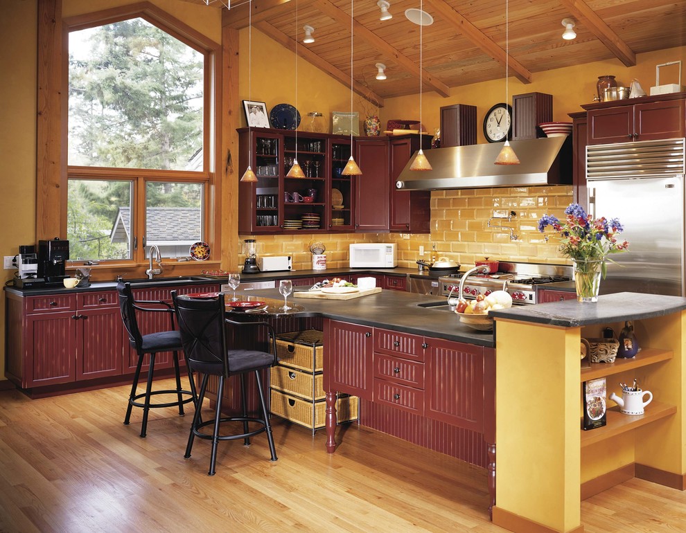 Foto på ett vintage l-kök, med rostfria vitvaror, skåp i slitet trä och gult stänkskydd